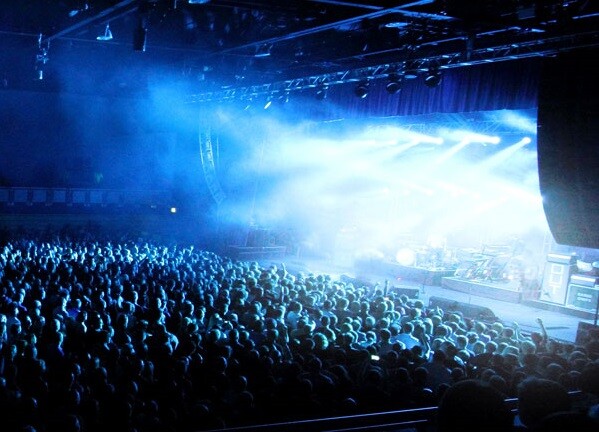 The interior of Grimsby Auditorium, with a large crowd cheering as blue light spills from a bright stage