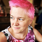 A headshot of Melody King, a non-binary individual with short vivid pink hair, wearing a floral top and smiling into the distance.
