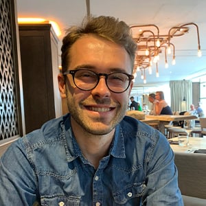 headshot of Robin Sheffield, a man with brown hair wearing a denim shirt and glasses, smiling into the camera